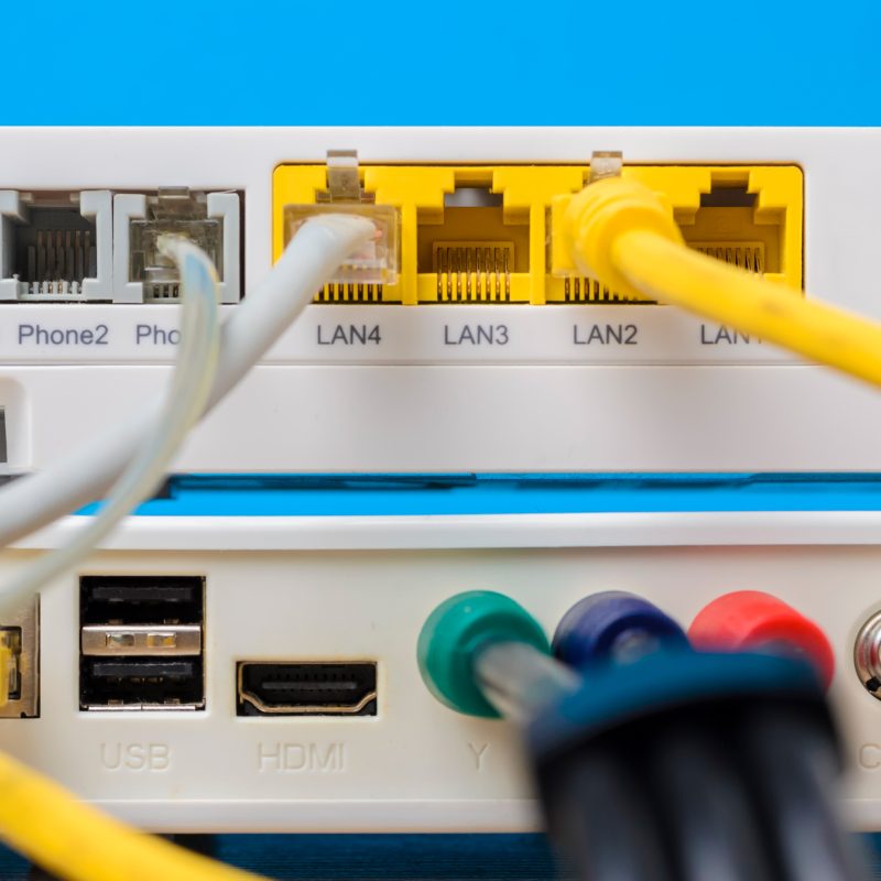 home wireless router with ethernet cables plugged in on blue background, close up