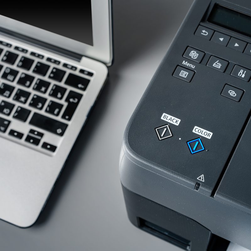 Printer and laptop on grey table in office close up